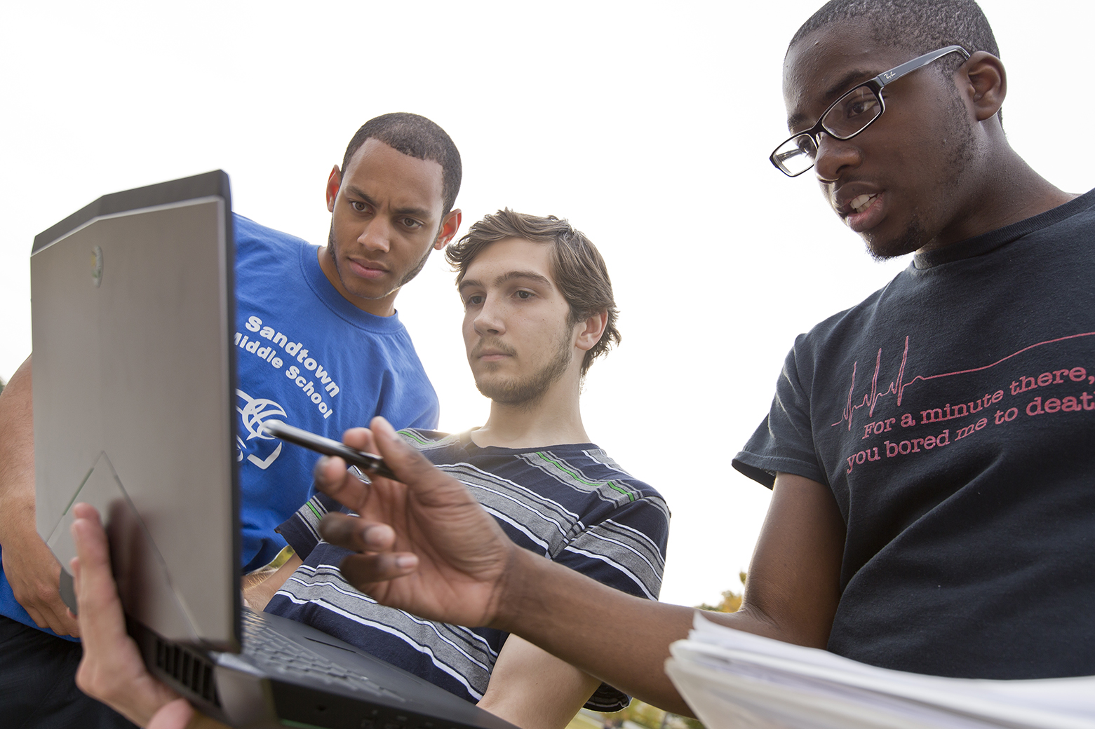 Three male students looking at a laptop computer. 