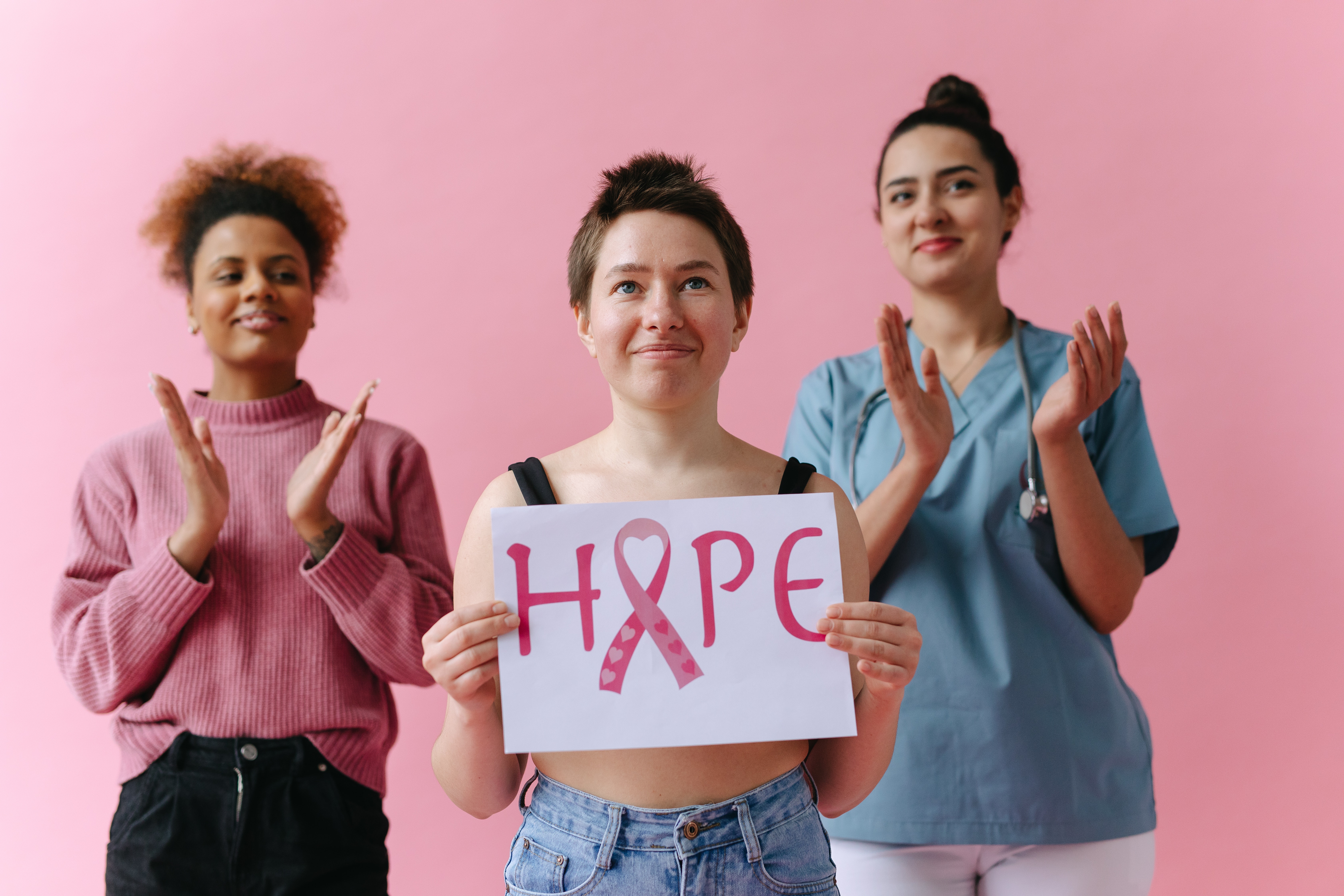 Woman holding a breast cancer awareness sign reading "hope" applauded by her friends